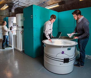 Chain of Custody Test Bed — Justin Fernandez (5943), left, adjusts an item monitor at Sandia’s Chain of Custody Development Test Bed where engineering development work supports eventual arms control technology experiments and demonstrations at NNSS. Mike Coram, center, and Jay Brotz (both 6831) work with a container used to store mock weapons during testing. 	(Photo by Randy Montoya)