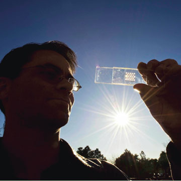Project lead Greg Nielson holds a solar cell test prototype with a microscale lens array fastened above it that together will help create a concentrated photovoltaic unit .  (Photo by Randy Montoya)