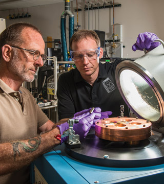 SHAPE MEMORY ALLOYS — Mark Reece (foreground) and Don Susan (both 1831) examine a new shape memory alloy button that they have removed from an arc-melter. Several new alloys have been developed at Sandia. For more about their groundbreaking work, see the story on page 8. (Photo by Randy Montoya)
