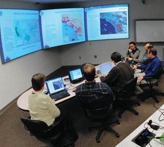 Image of <p>NISAC TEAM — A NISAC team of infrastructure modelers and analysts works on providing a crisis response to the Department of Homeland Security. When NISAC is activated, such teams provide quick analyses to DHS for national events such as hurricanes.  (Photo courtesy of NISAC)</p>