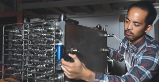 Image of <p>Adrian Narvaez of Hawaii Hydrogen Carriers (HHC) observes a metal hydride storage tank, part of a project led by Sandia. The tank will be combined with a fuel cell system to make a fuel cell power pack to power a forklift. Hydrogen fuel cell technology could have a significant advantage over batteries for a large slice of the $33 billion US forklift market.  (Photo by Dino Vournas)</p>