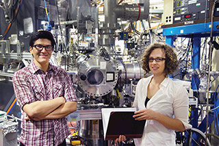 COMBUSTION SLEUTHS — John Savee (8353), left, identified cycloheptadiene as the best fuel for creating a detectable QOOH, and Sandia computational expert Ewa Papajak (8353), right, and her adviser, Judit Zádor, used quantum chemistry to explain the mechanism of the reaction. John and Ewa appear in front of an instrument, the Multiplexed Photoionization Mass Spectrometer in the Advanced Light Source at Lawrence Berkeley National Laboratory, that took direct measurements. 	(Photo by David Osborn)
