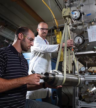 Image of <p>In the Hydrogen Effects on Materials Laboratory, Joe Ronevich, left, and Jeff Campbell (both 8252) use a crane to maneuver a stainless steel pressure vessel containing material test specimens into place before connecting it to the manifold piping and filling it with high-pressure hydrogen gas.  (Photo by Dino Vournas)</p>