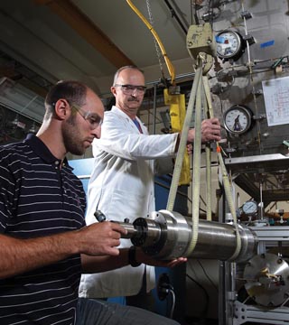 In the Hydrogen Effects on Materials Laboratory, Joe Ronevich, left, and Jeff Campbell (both 8252) use a crane to maneuver a stainless steel pressure vessel containing material test specimens into place before connecting it to the manifold piping and filling it with high-pressure hydrogen gas. (Photo by Dino Vournas)