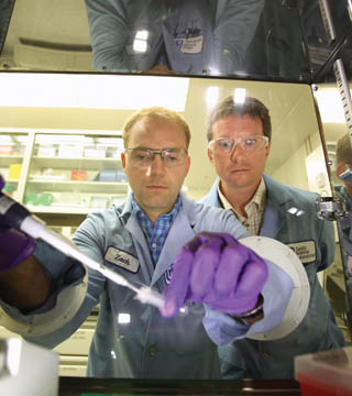 Zach Bent, in the foreground with Steve Branda, manipulates a pathogen capture reaction under high temperature to maintain stringent hybridization conditions so that binding specificity remains high, thus enhancing efficiency of the capture. (Photo by Dino Vournas)