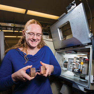 Lisa Deibler (1819) holds a tubing specimen in a grip, ready to load it into the thermal-mechanical experimental system behind her. Lisa of Sandia/New Mexico and Arthur Brown (8259) of Sandia/California worked together to develop a simulation for an annealing process to soften tubing that was too hard for the requirements of the job. (Photo by Randy Montoya)