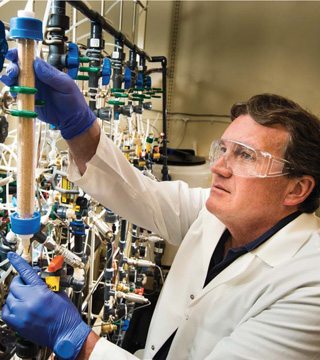 The permeable reactive barrier’s inventor, Bob Moore, examines the apatite barrier forming during a lab test. (Photo by Randy Montoya)