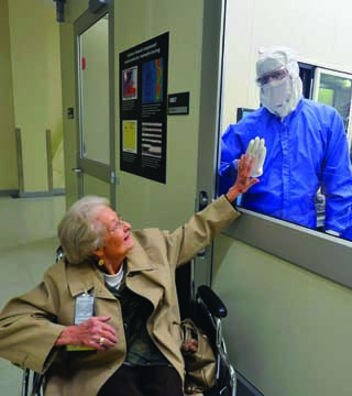 TOUCHING MOMENT — Belva Whitfield, widow of Sandia legend Willis Whitfield, inventor of the laminar airflow cleanroom, gets a gentle greeting from a Sandian in a cleanroom in Sandia’s MESA complex. Willis will be inducted posthumously into the National Inventors Hall of Fame in May. (Photo by Randy Montoya)