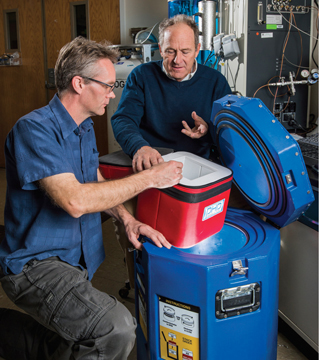 Physical chemist Eric Coker (1815), left, looks over shipping containers developed by Santa Fe businessman Bruce McCormick, right, that safely transport and store temperature-sensitive vaccines and biopharmaceuticals. Eric helped McCormick create a solar thermal icemaker to provide cooling for the containers. They worked together through the New Mexico Small Business Assistance Program. (Photo by Randy Montoya)
