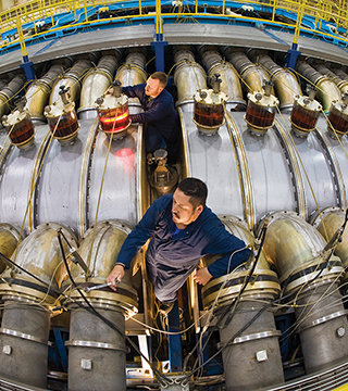 Former contractor JJ Montoya (foreground) and Chris Kirtley (1342) work atop the HERMES III Accelerator, making final adjustments on a newly rebuilt cavity.  (Photo by Randy Montoya)