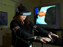 VIRTUAL CASUALTY Lydia Tapia of Proliferation Sciences Dept. 5913 demonstrates BioSimMER, a virtual reality application developed at Sandia that soon will allow rescue personnel to practice responding to a terrorist attack involving release of a biological warfare agent. Through her goggles, Lydia sees the scene that is displayed on the screen behind her. The virtual patient she is treating suffers from a severe head wound and exhibits realistic symptoms, such as heavy breathing and rapid eye movement. If Lydia doesn't administer the proper medical procedures in time, the patient will die. (Photo by Randy Montoya)Download 150dpi JPEG image, 'vr_pix.jpg', 1 Mb