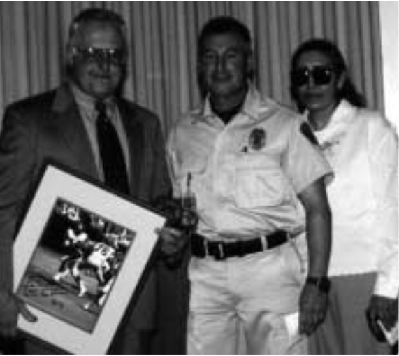 THANK YOU, CHARLIE — Michael Tachias, middle,and Josephine Chavez (both 7140), right, present anautographed picture of former Cincinnati Bengalsquarterback Kenny Anderson to Charlie Emery duringCharlie’s retirement party Jan. 31. The picture came asa surprise and was a reminder of one of Charlie’s ear-lier careers — college football coach. Charlie coachedAnderson at Augustana College in Illinois.