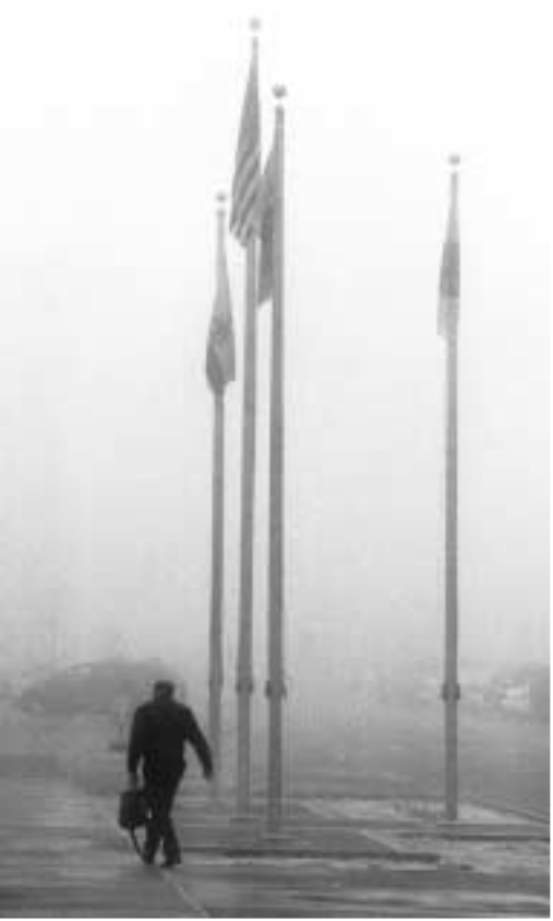 WINTER SURPRISE — Dense, cold fog greeted Sandians and all Albuquerque residents on the morning of Jan. 24. Here a Sandian trudges past the nearly indistinguishable flagpoles in front of Bldg. 800. The foggy morning was just the beginning of a more than week-long period of cold, snow, and wind throughout much of New Mexico, as real winter returned for the first time in several years.