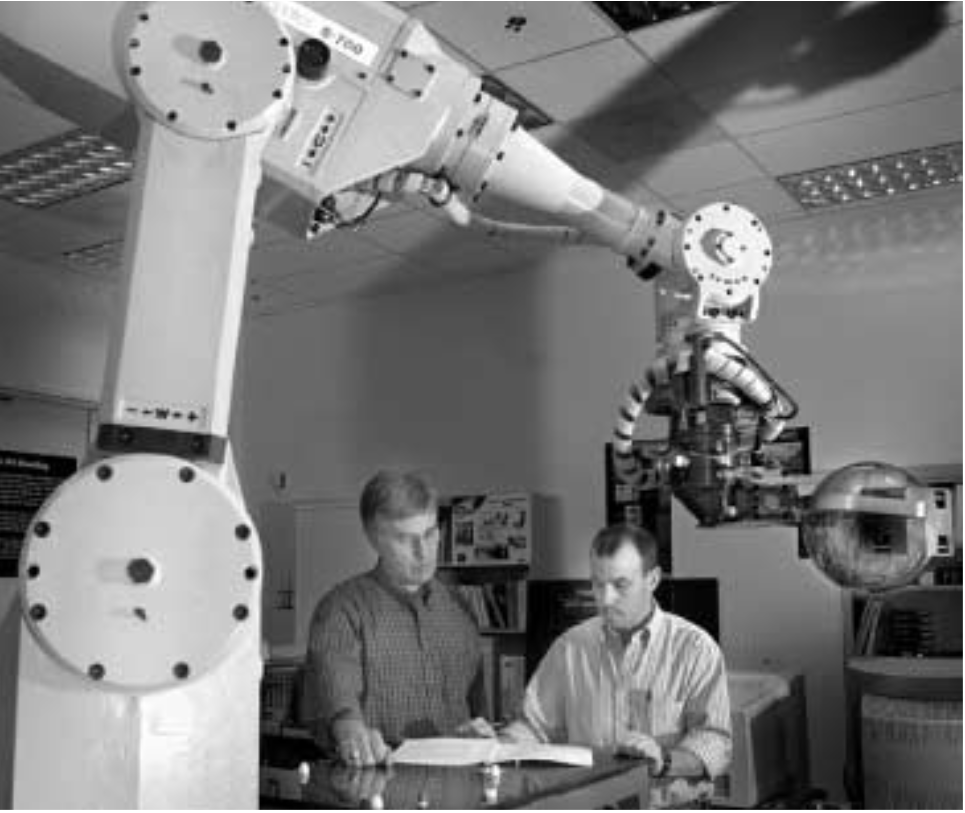 PIT BOT — Bill Drotning, left, and Howard Kimberly with a developmental pit-handling system at Sandia similar to the automated Weigh and Leak-Check System (WALS) now at Pantex. The robot is seen grasping a bowling ball. (Photo by Randy Montoya)