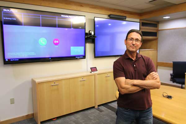 Image of Dave Nagel stands with equipment he installed in a Sandia conference room