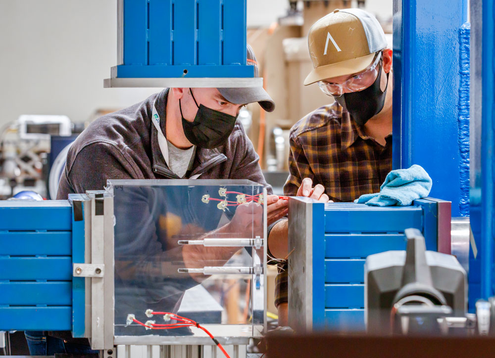 Image of Sandia engineers examine a plexiglass cube fractured by a small-scale explosion