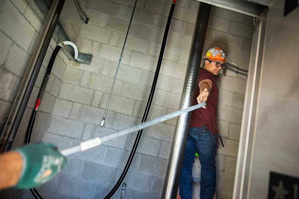 LEVEL UP — Electrician Felipe Diaz grabs a length of conduit while installing an elevator at Building 800. The elevator is designed to operate with less power than the one it replaced. (Photo by Craig Fritz)