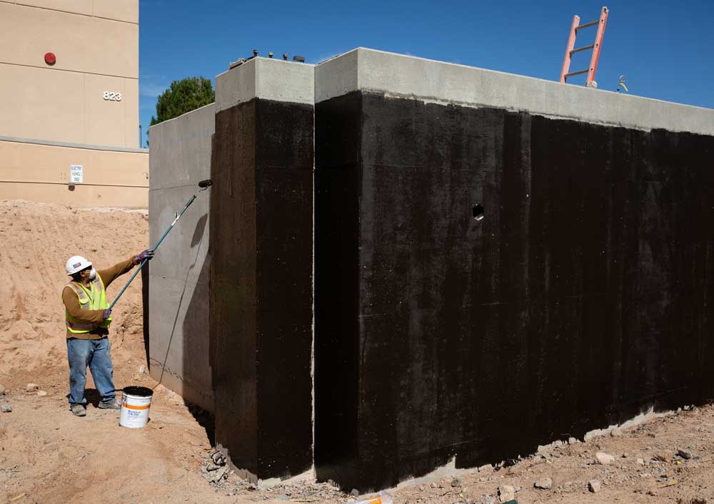 POWER UPGRADES — Ramon Silva applies sealant to pits to hold water and support for a new cooling tower that will replace the one on top of Building 823. The new towers will be ground level and use less power to operate. (Photo by Craig Fritz)