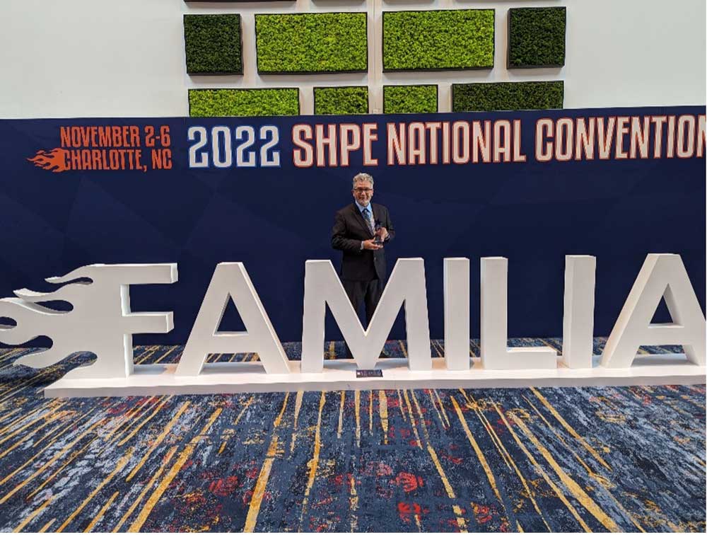 Image of Rudy Garcia stands behind a structure that says "familia" at the Society of Hispanic Professional Engineers national conference