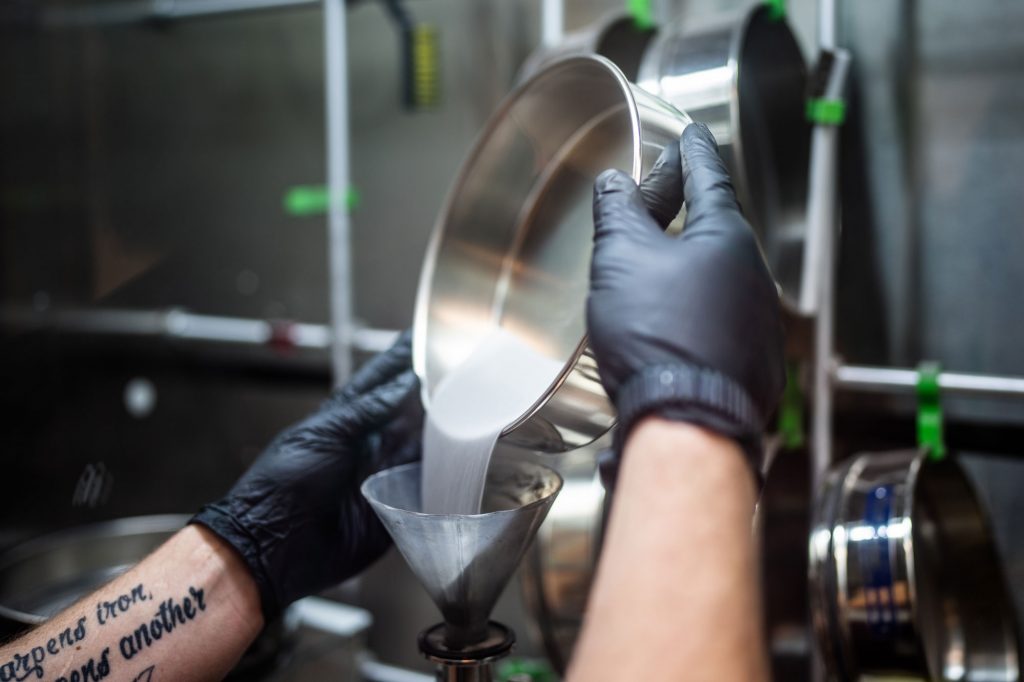 POUR ME ANOTHER — Sandia technologist Levi Van Bastian fills a hopper with raw material to print on the Laser Engineered Net Shaping machine. What appears to be a liquid is powdered metal. (Photo by Craig Fritz)