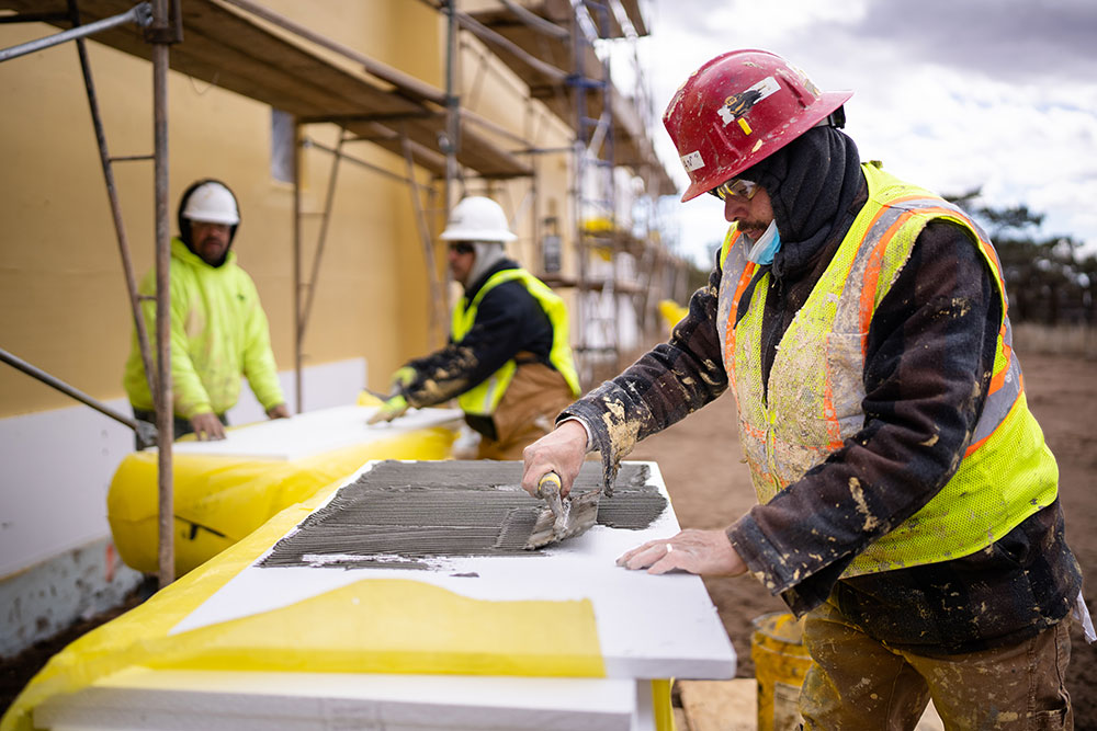 LEVELING UP — Cruz Duran works with plaster while insulating a maintenance garage in Eldorado, New Mexico, as part of a Pluma project. (Photo by Craig Fritz)