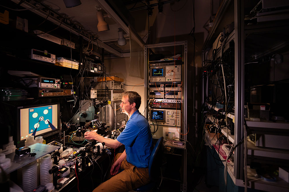 SHRINKING GAME —Darwin Serkland is developing novel microscopic semiconductor lasers for use in next-generation atomic clocks at Sandia. Needle probes positioned under a microscope drive 2 milliamps of current into a laser diode, which produces almost 1 milliwatt of monochromatic light at a wavelength of 894 nanometers. The laser diode shown here is a hundred times smaller than a grain of salt. (Photo by Craig Fritz)