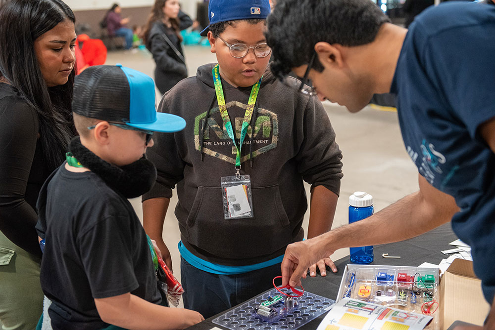 THE BASICS OF ENGINEERING — Postdoctoral appointee Aditya Venkatraman, right, uses a snap circuit to demonstrate electronics and circuitry concepts to students at the Discovery Festival on Nov. 17. The annual event, hosted by Big Brothers Big Sisters of Central New Mexico and sponsored by Sandia, introduces K-12 students to businesses and job opportunities through interactive activities and discovery. (Photo by Daniel Roth)