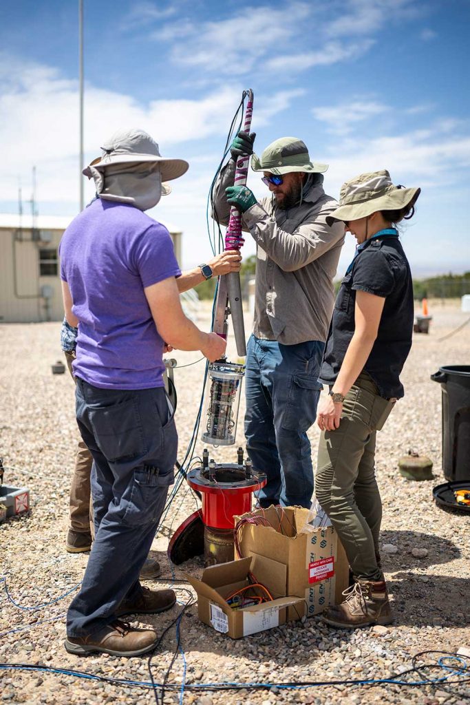 DOWN THE WELL — From left to right, electronics engineer Alfred Cochrane, electromechanical technologist Taylor Myers and mechanical engineer Melanie Schneider position a downhole acoustic transceiver and energy harvesting tool before lowering it into a well.