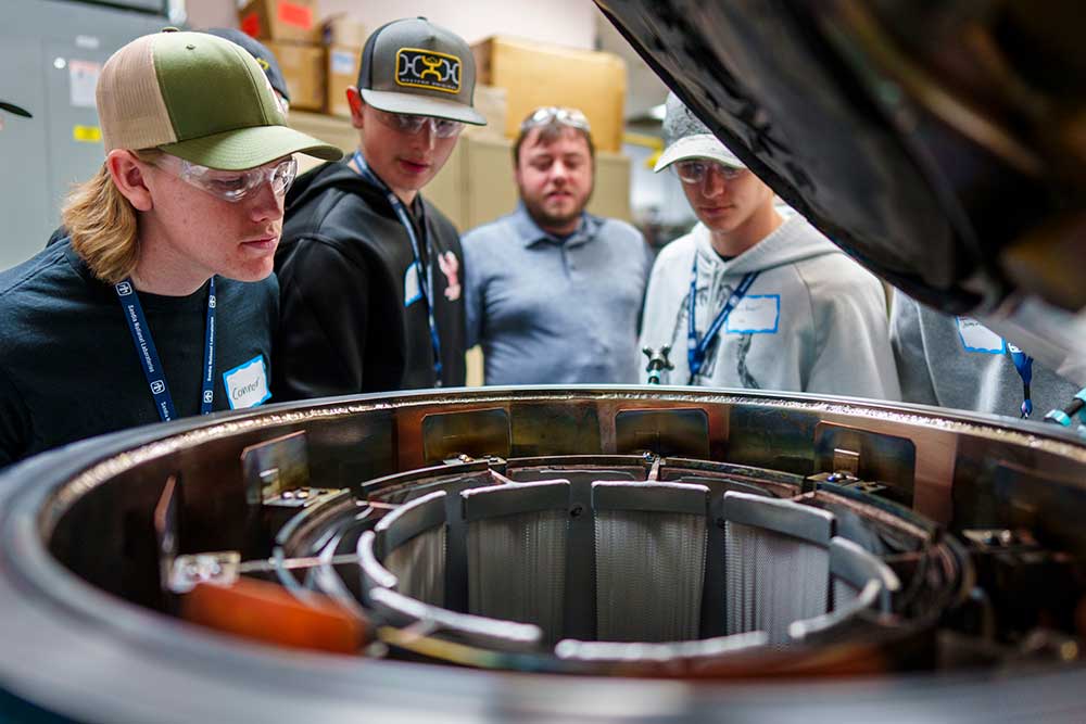 LOOKING INSIDE THEIR FUTURE — Rio Rancho students Connor Rosenson, Donn Palmer and Archer Mount, left to right, look into an oven containing critical welding components, as explained by Joshua Guggino, back. (Photo by Craig Fritz)