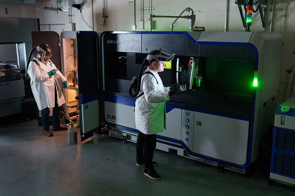 VALUE ADDED — Electromechanical technologists Joe Olguin, left, and Brandon Langdon work on a new selective laser melting 3D printer at the Sandia California Additive Manufacturing Lab. (Photo by Craig Fritz)