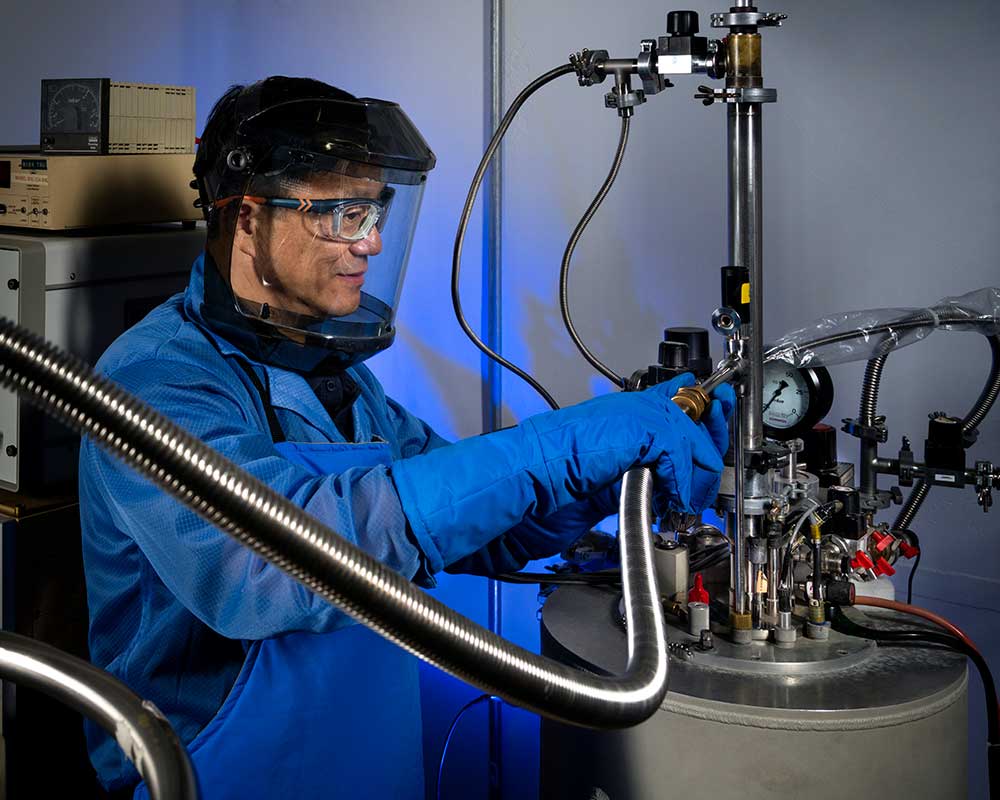 SMALL STUDIES, BIG IMPACT — Wei Pan, performing a liquid helium transfer, turned a fascination with the smallest forms of matter into a career redefining how they are studied. (Photo by Randy Wong)