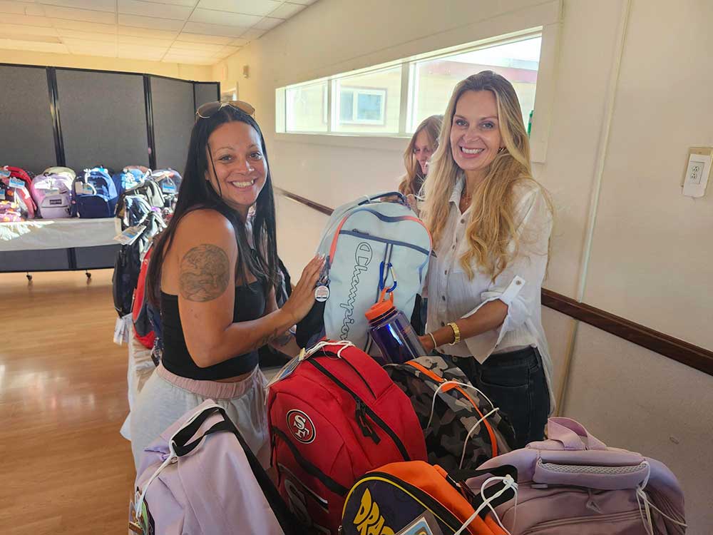 SUPPLIES AND SMILES — Executive Assistant Rachel Sowell, right, coordinated an effort to distribute backpacks to 108 military families.