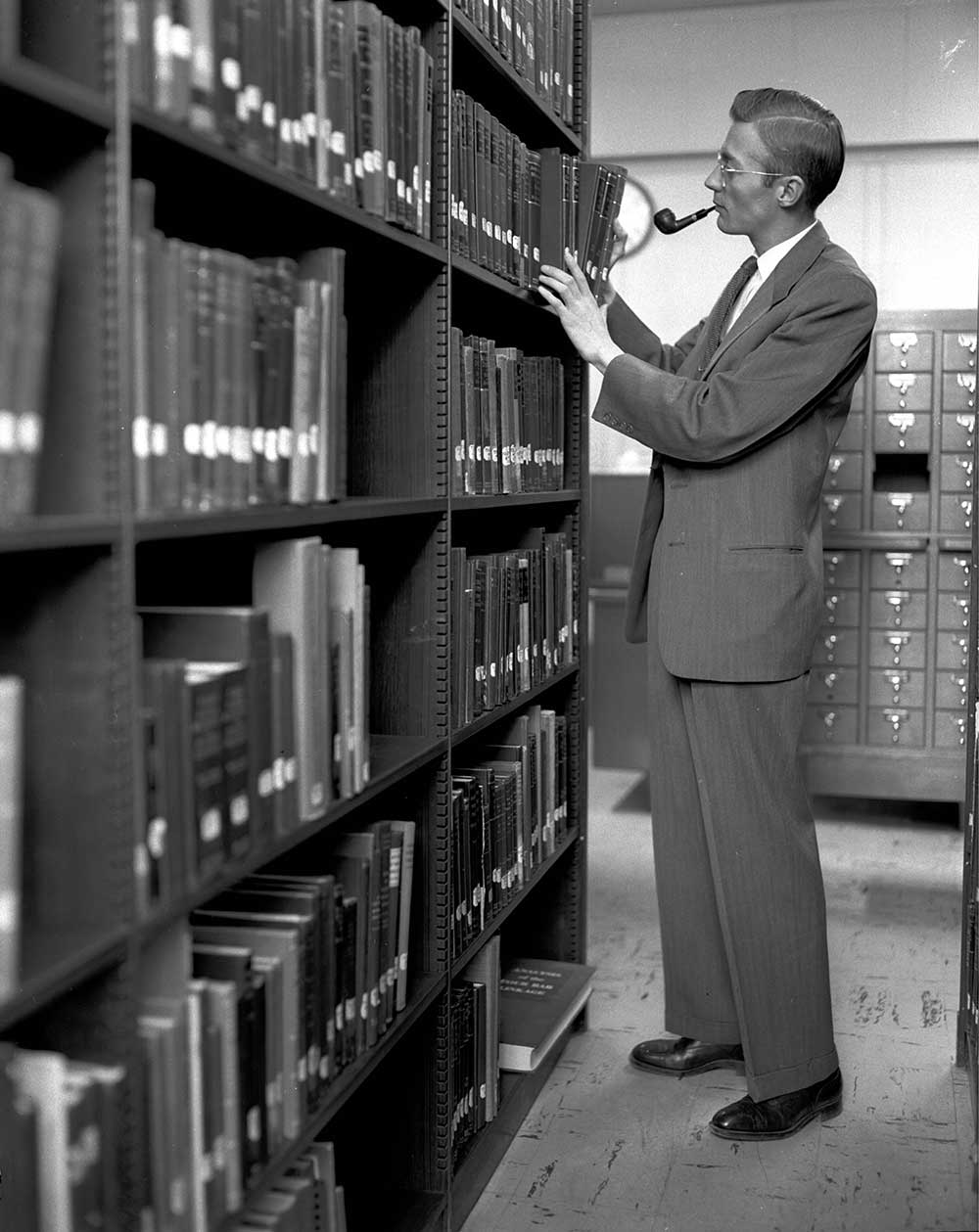 SORTING THROUGH THE STACKS — The head librarian shelves books, pipe in tow, in a 1953 photo. (Photo from the Lab News archives)