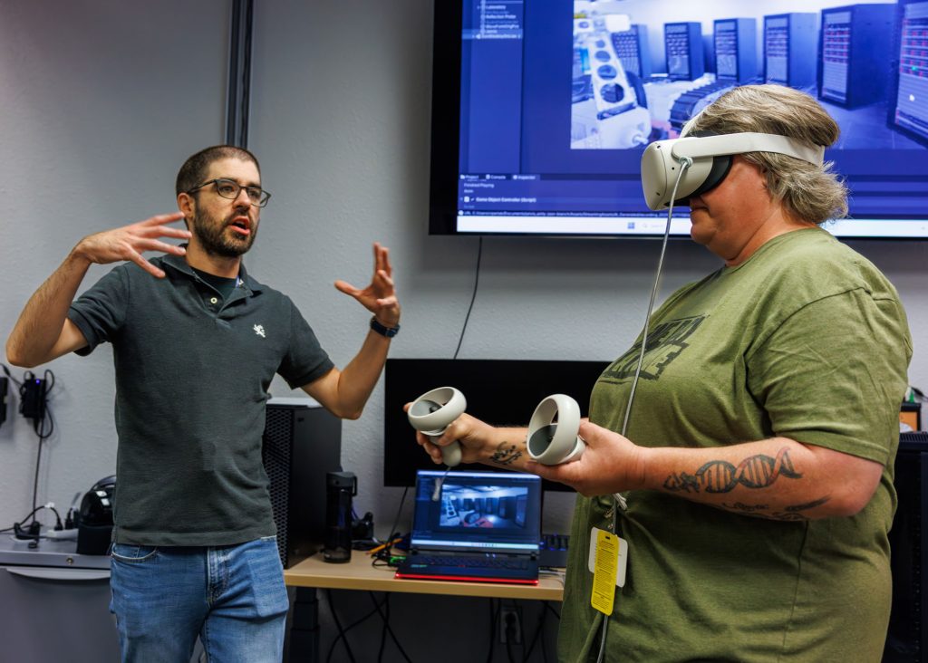 <strong>AUDIBLY IMPRESSIVE </strong>— Danny Gomez, a former applied machine intelligence expert at Sandia, coaches Yucca Middle School teacher Laura DeBusk through a demonstration of JARVIS, a virtual reality environment that uses AI to answer users’ questions with real-time, audible answers in natural language. (Photo by Bret Latter)