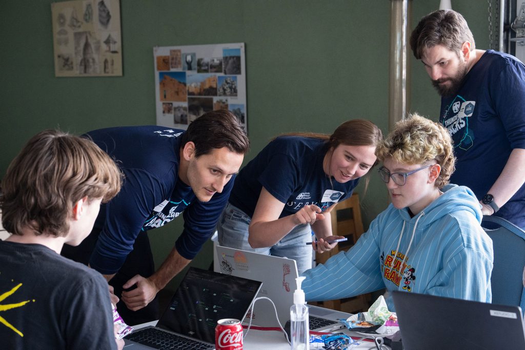 <strong>AI ASSIST </strong>— From left, Sandia volunteers Nathan Brown, Catherine Appleby and Ben Feinberg work with Katherine Dahringer, a junior at Explore Academy, during Thunderbird Hacks on Jan. 31. (Photo by David Lienemann)