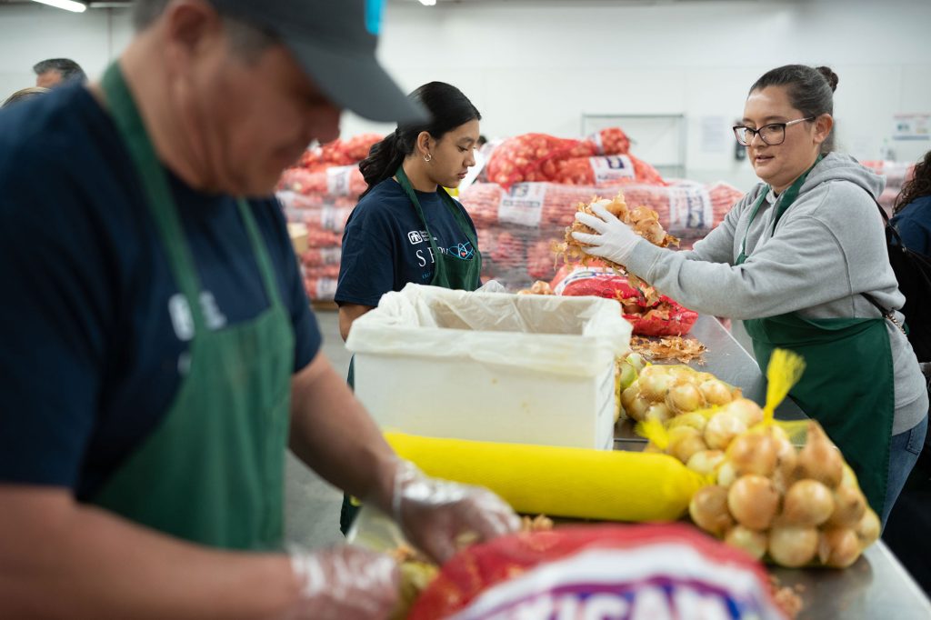 <strong>SMOOTH OPERATION </strong>— From left, engineering project lead Bob Pacheco, Mariah Ramirez and her mother, auditor Ashley Ramirez, sort and pack 50-pound bags of onions during a service project at Roadrunner Food Bank on April 25. (Photo by David Lienemann)