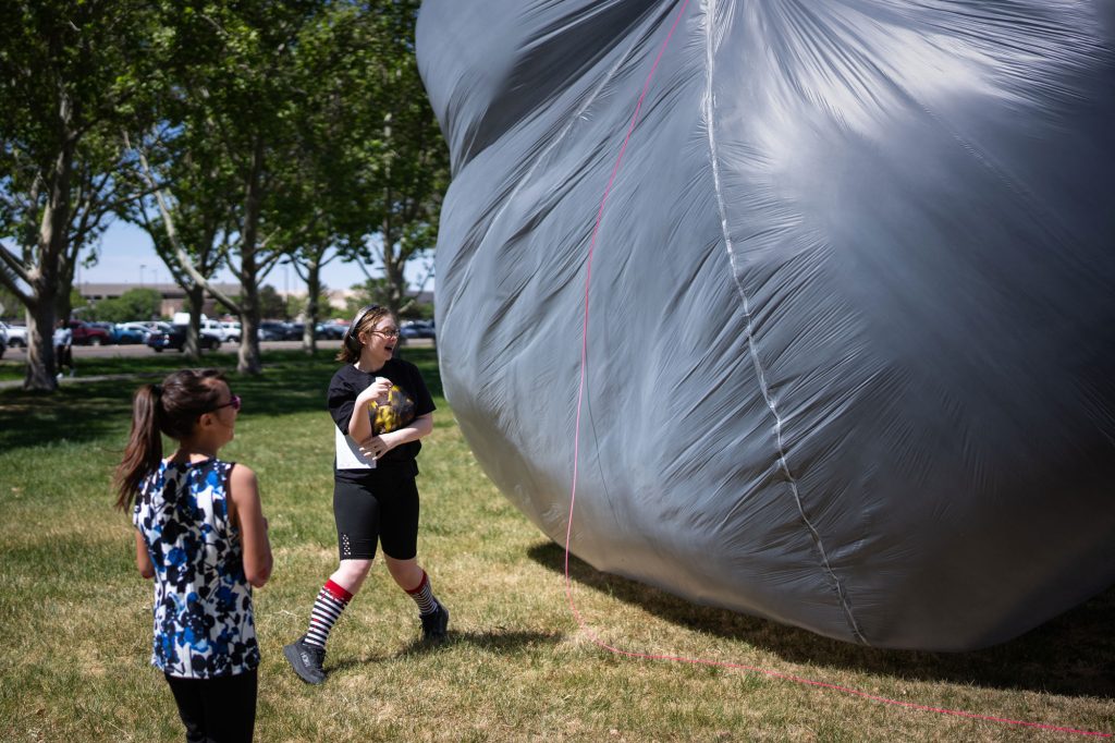 <strong>UP, UP, OUT OF THE WAY</strong> — Lucia Alvorez, 12, left, and Katy Orona, 13, avoid a wind-blown high-altitude solar balloon inflated by Atmospheric Science team members at Hardin Field during Kids Day. Staff members organized 70 activities across the New Mexico site, from the solar tower to Hardin Field.