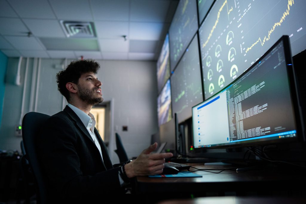 <strong>CONTROL ROOM </strong>— Sandia engineer Rachid Darbali-Zamora monitors an AI-driven distributed energy resource management system in the control room at Sandia’s Distributed Energy Technologies Laboratory. The dashboard displays real-time controls designed to help keep voltage within operating limits as grid conditions change.<br>(Photo by Craig Fritz)