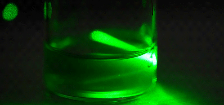 <strong>SCATTER SHOT</strong> — A vial of nanosheets formed from lithium battery cathodes in water by Sandia’s battery upcycling method. The scattered light from a green laser indicates that the cathodes have been successfully broken down into nanosheets. (Photo by Craig Fritz)
