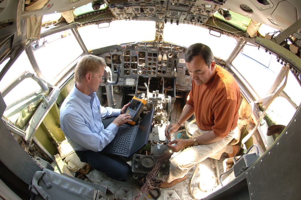 <strong>WIRING DIAGNOSTIC </strong>— Sandians Larry Schneider, left, and Mike Dinallo prepare to employ the Pulse Arrested Spark Discharge diagnostic in 2006 on a wiring bundle in the cockpit of a retired Boeing 737. (Photo by Randy Montoya)