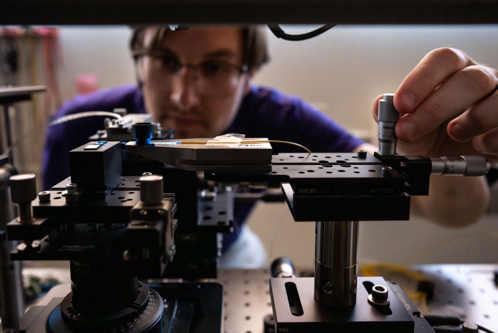 <strong>ALL LINED UP</strong> — Sandia photonics researcher Forrest Hubert aligns an experimental chip with an optical waveguide carrying laser light. Sandia collaborates with quantum computing company Quantinuum to develop and test similar technologies.
