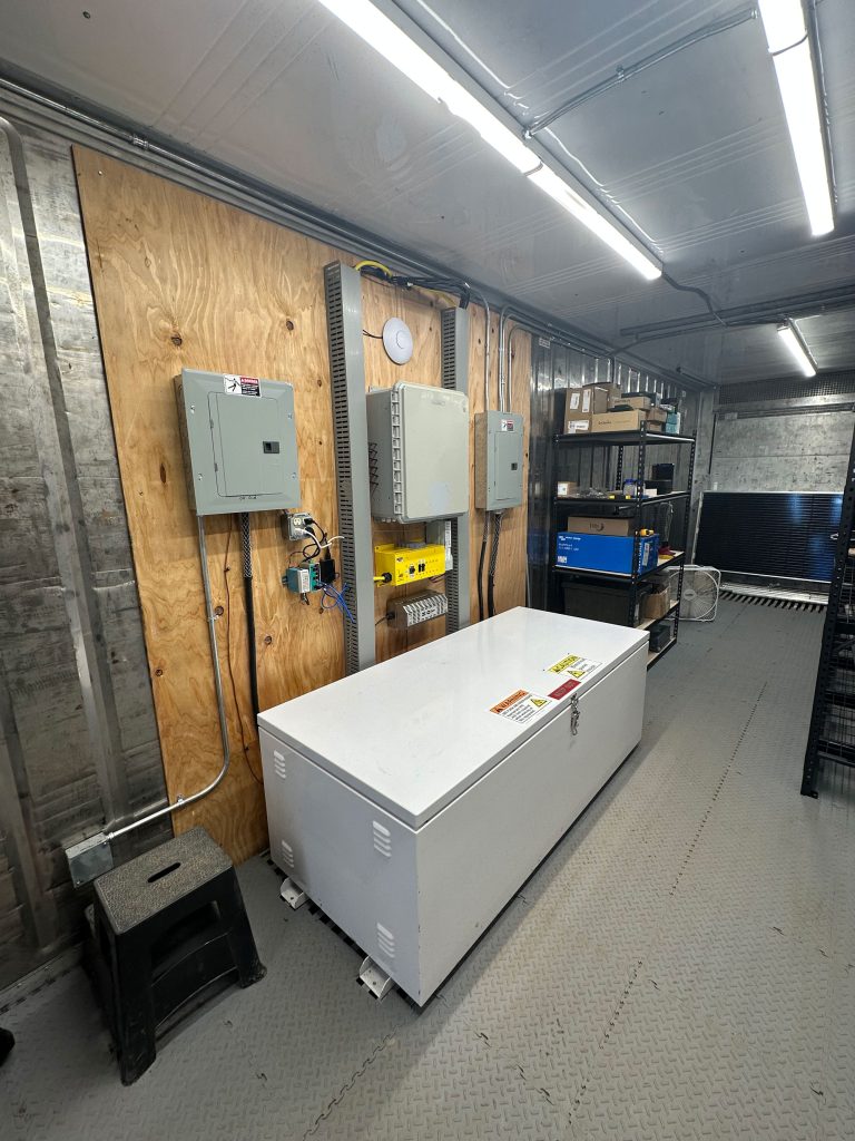 <strong>OUT OF THE BOX </strong>— The shipping container beneath the solar array contains the photovoltaic system’s datalogger, inverter, battery bank for energy storage and additional components. (Photo by Justin LaPierre)