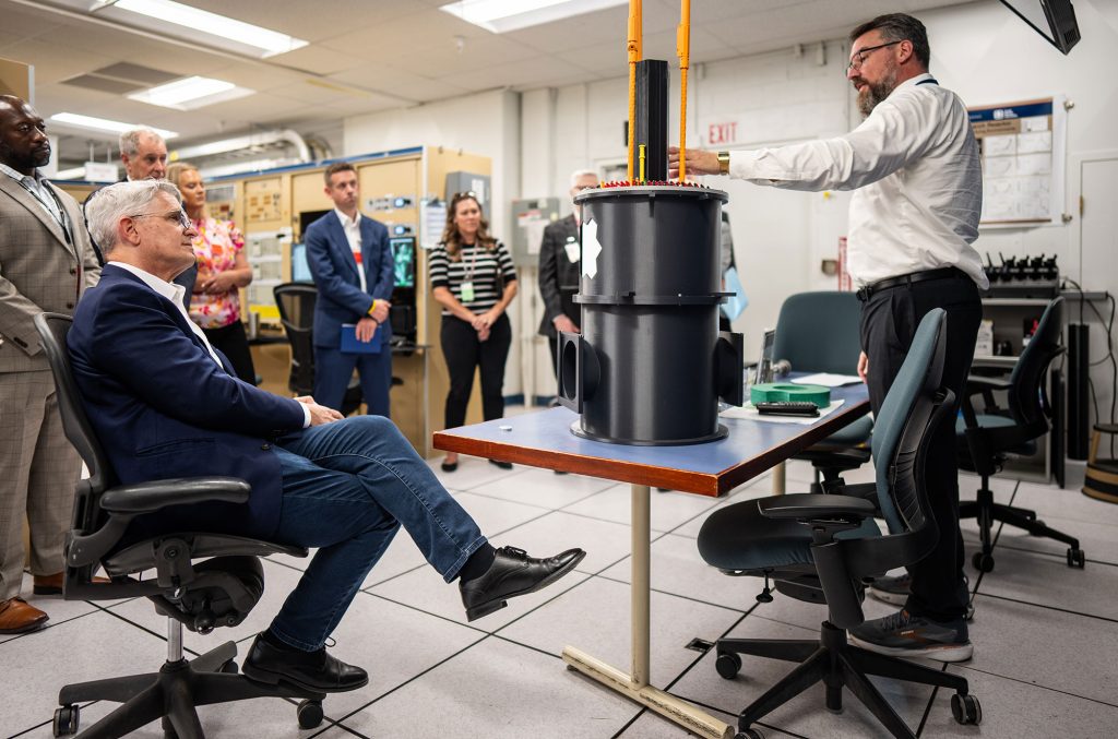 <strong>REACTOR RUNDOWN</strong> — NNSA Administrator Brandon Williams, left, listens as Sandia senior manager David Epp, right, provides a briefing on the Annular Core Research Reactor during Williams’ visit to the Labs on Aug. 24. A model of the reactor sits on the table between them. During his visit, Williams also toured the Microsystems Engineering, Science and Applications facility and received briefings on Sandia’s work and its critical impact on national security.