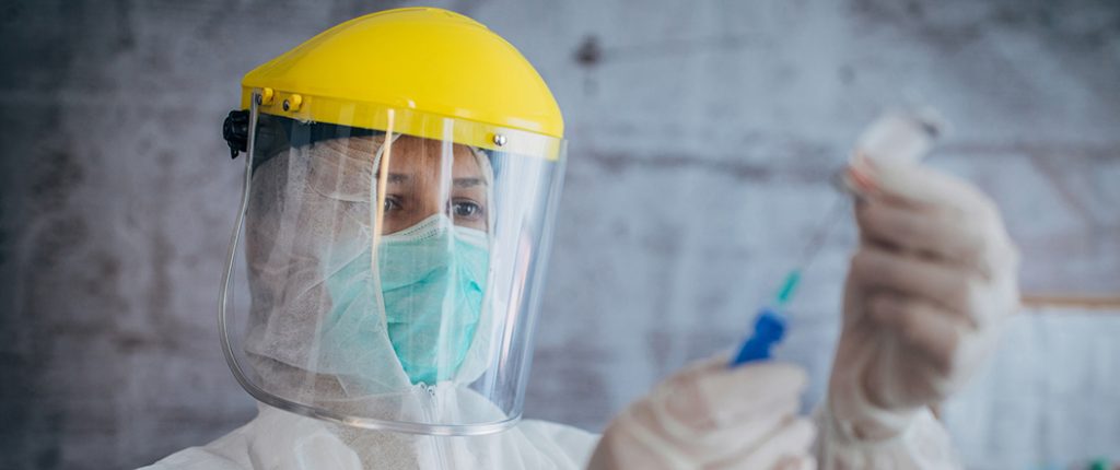 Image of Female doctor in protective suit holding syringe and tube